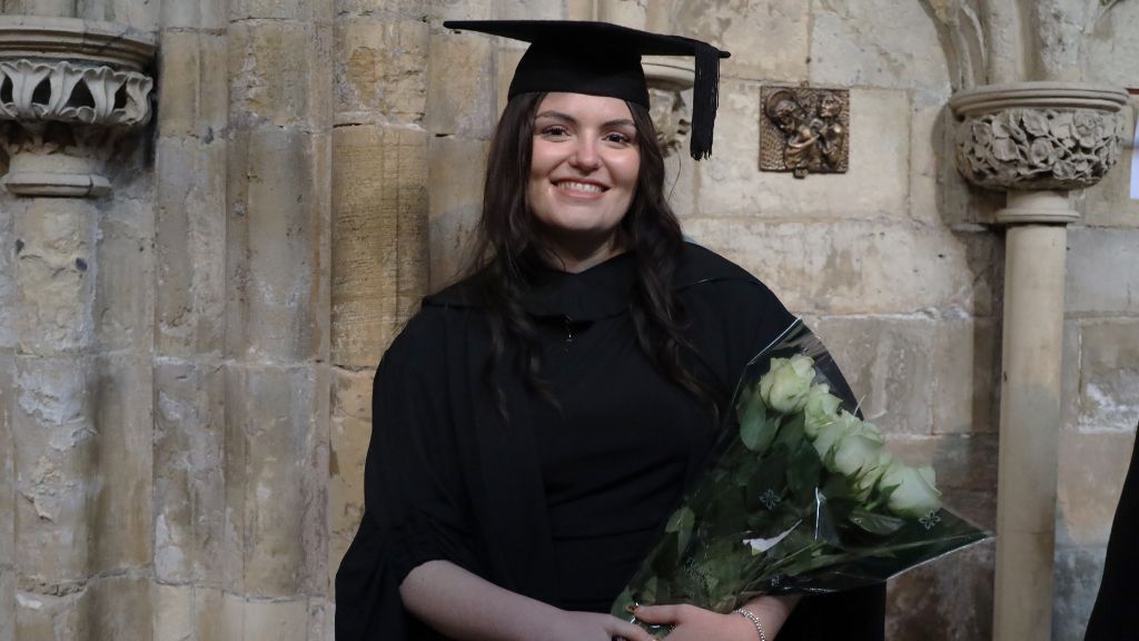 Student with a cap and gown holding flowers